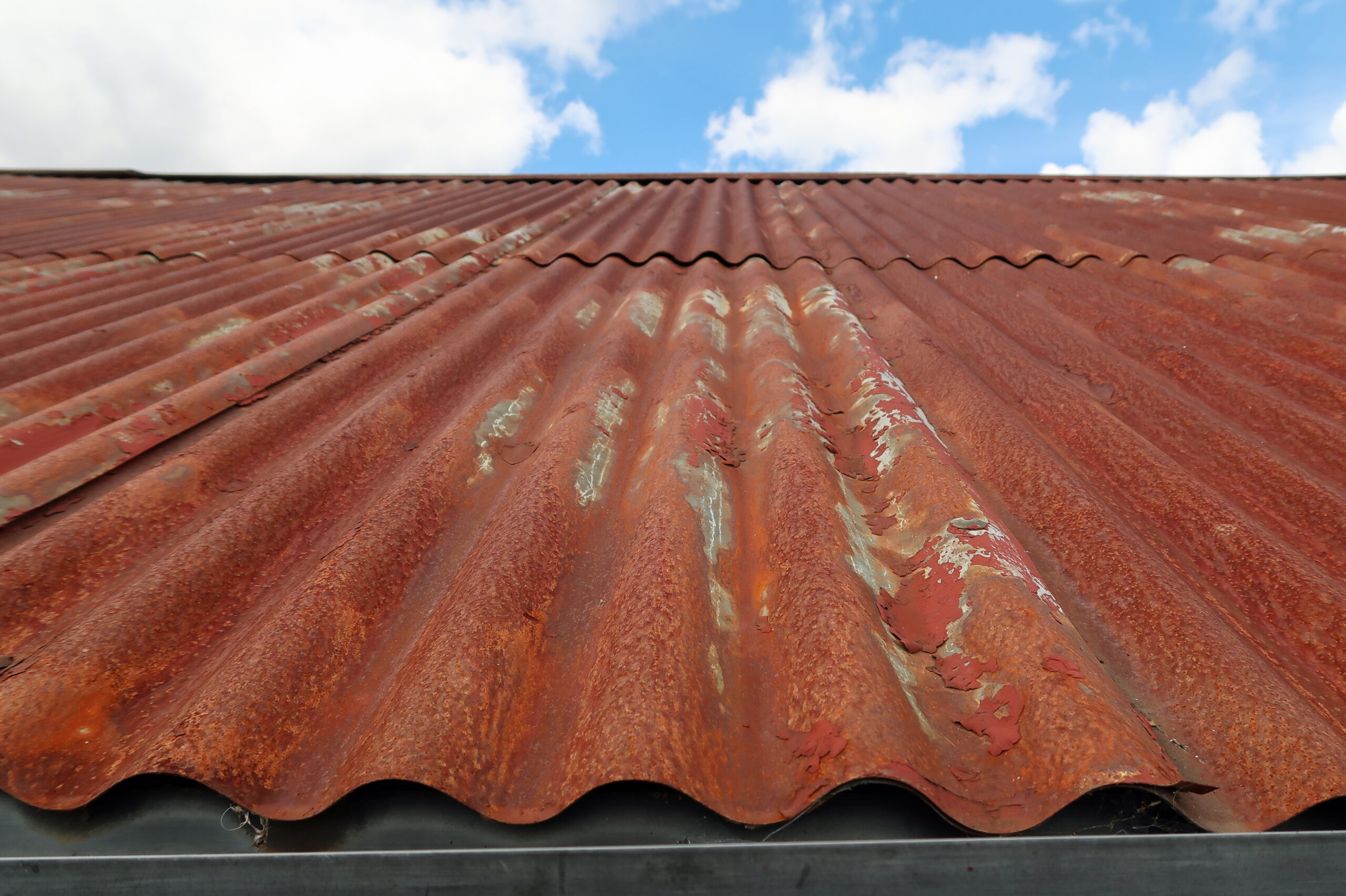 Red brown rusty corrugated iron roof without proper paint, primers, and coatings.