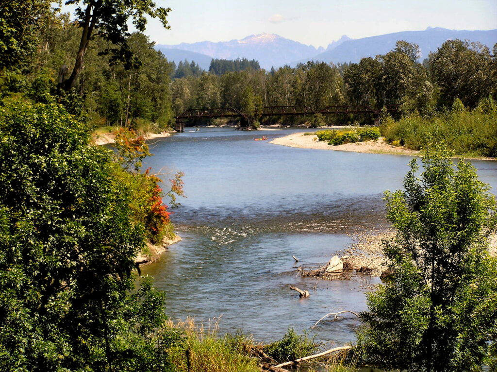 A scenic view of the Skykomish River with trees, beach areas, and a bridge in the distance.